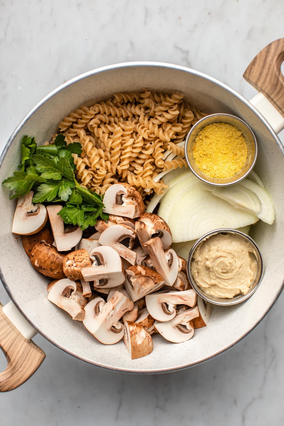 ingredients for one pot mushroom stroganoff arranged in large white pot on marble background