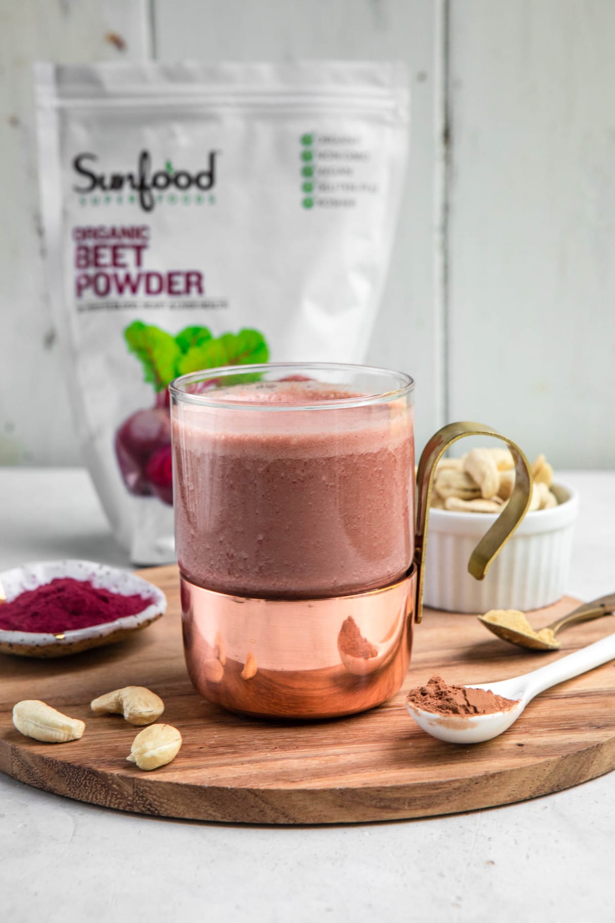 frothy beet latte in glass mug with bag of sunfood beet powder in the background