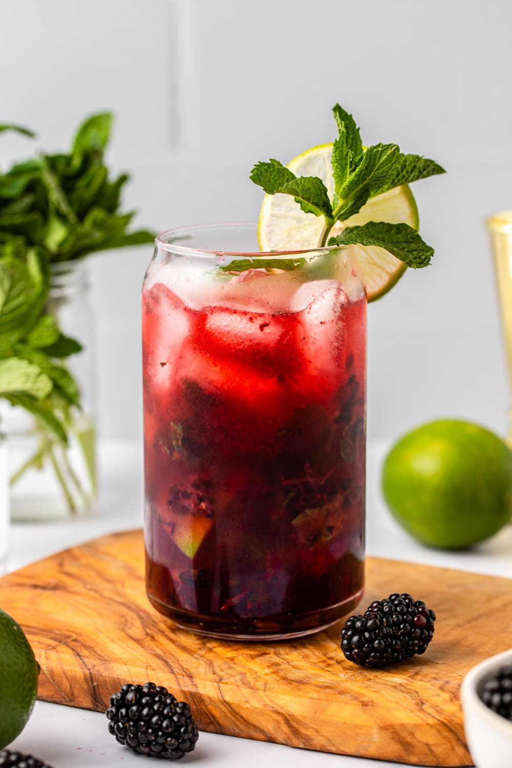 a zoomed in image of blackberry mojito served in a glass cup on a wooden board and decorated with berries and lime