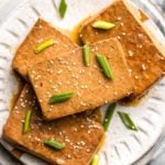 braised tofu on white plate topped with green onion and sesame seeds