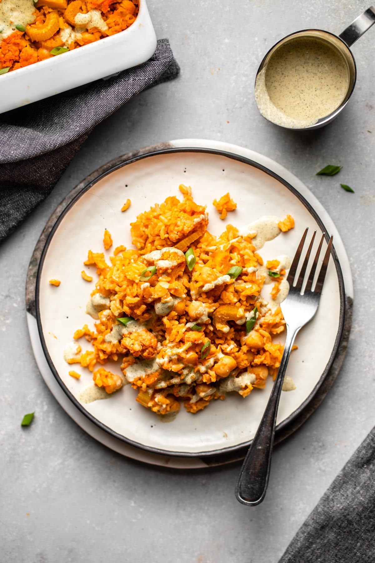 buffalo cauliflower and chickpea casserole topped with vegan ranch on white plate on grey background