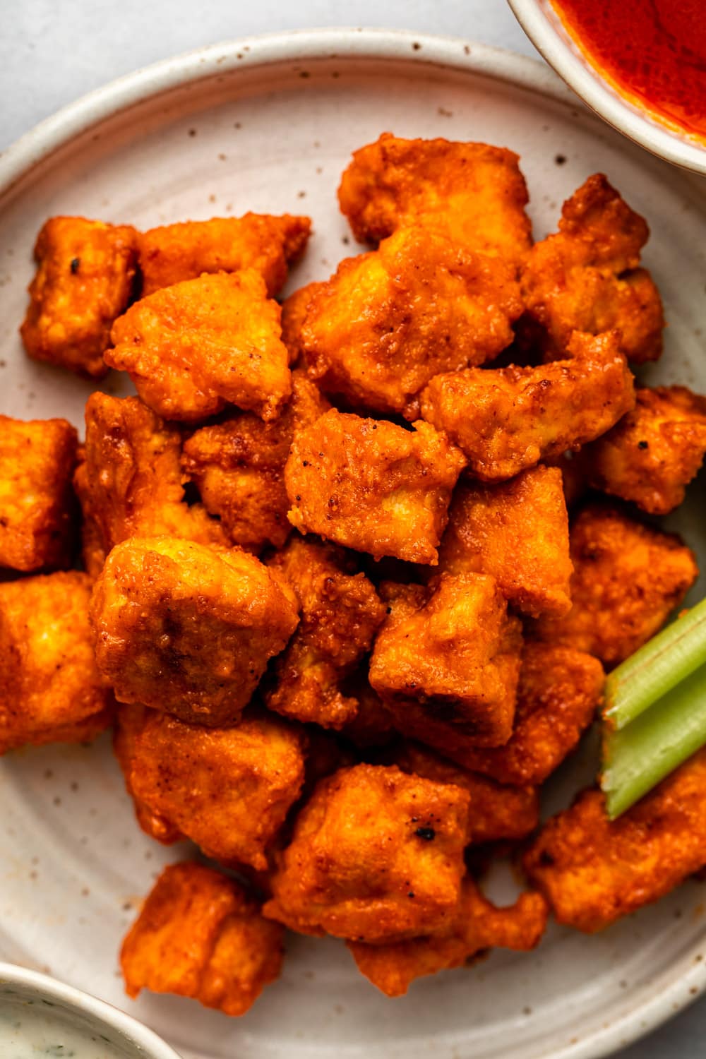 a zoomed in image of buffalo tofu bites served on a plate with celery sticks