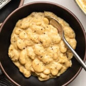Cacio e pepe butter beans in black serving bowl with silver spoon