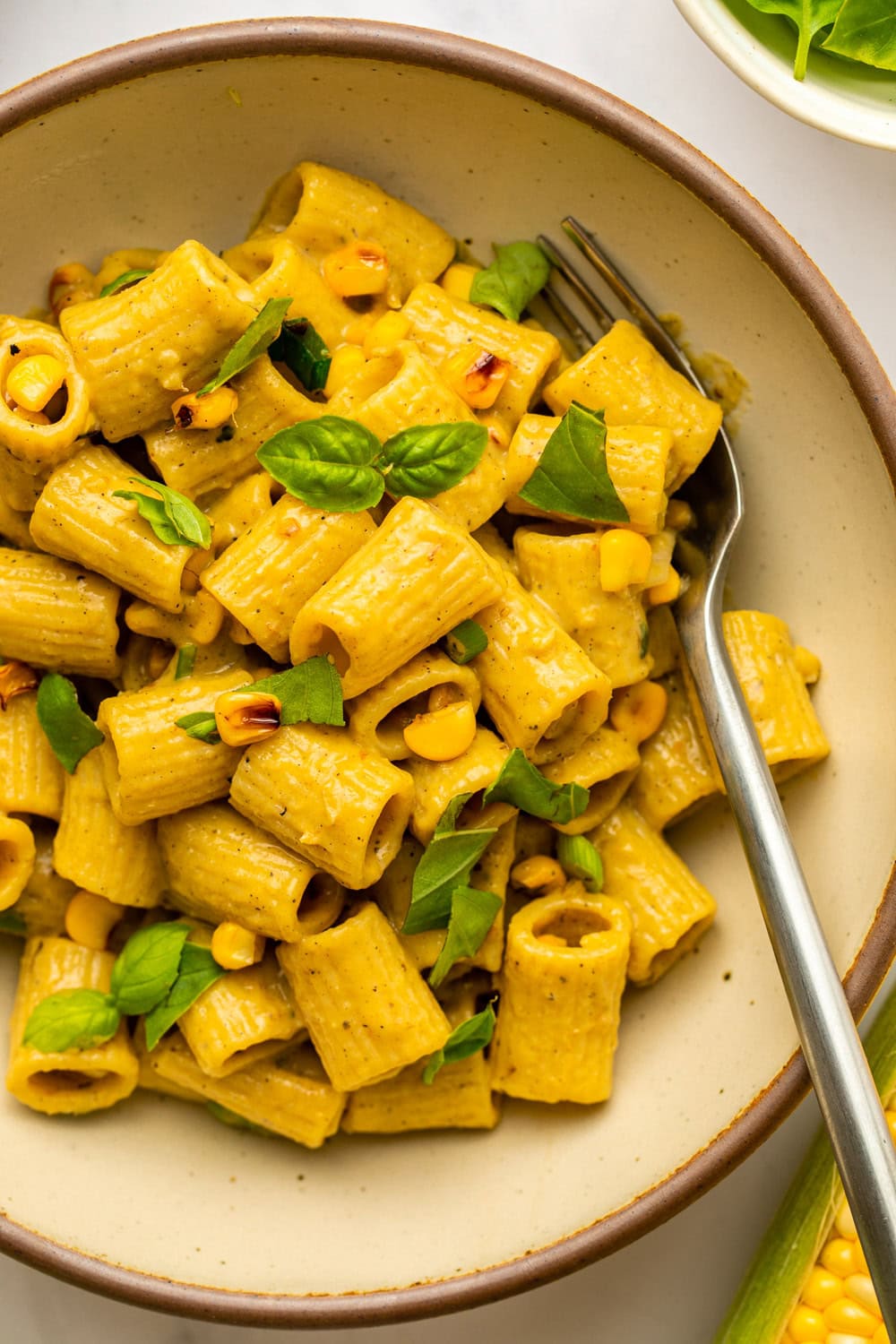 a zoomed on photo of corn basil pasta served on a plate with a fork on the side