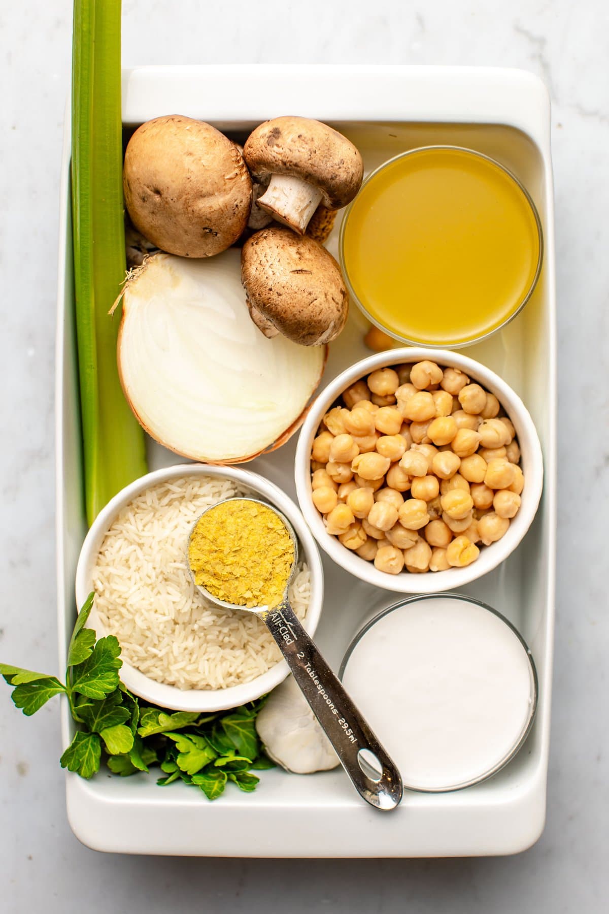 ingredients for chickpea rice casserole arranged in white casserole dish on marble background