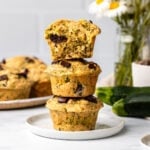 stack of 3 zucchini muffins on white plate with more muffins in the background