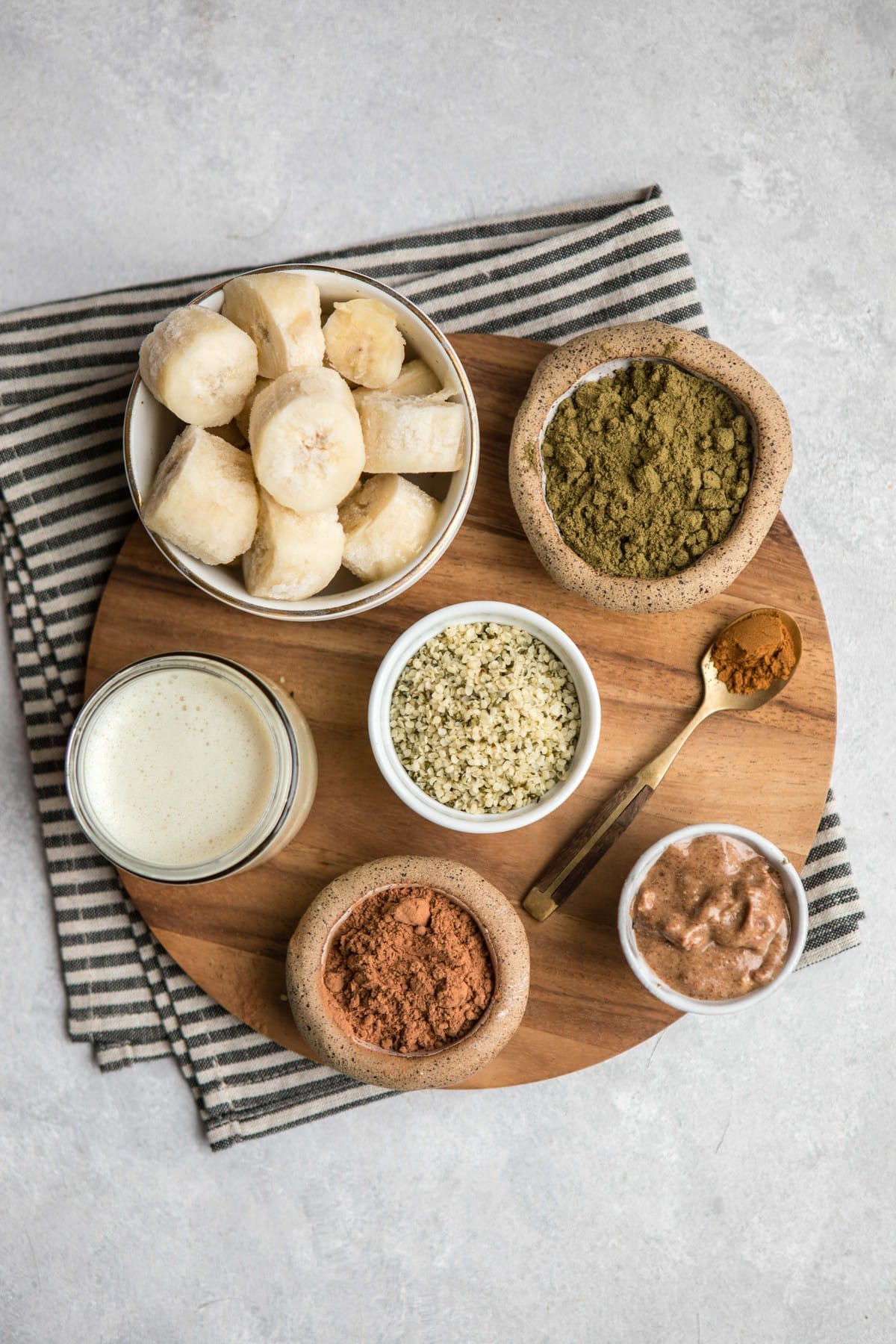 ingredients for chocolate hemp smoothie in small containers spread on wooden cutting board