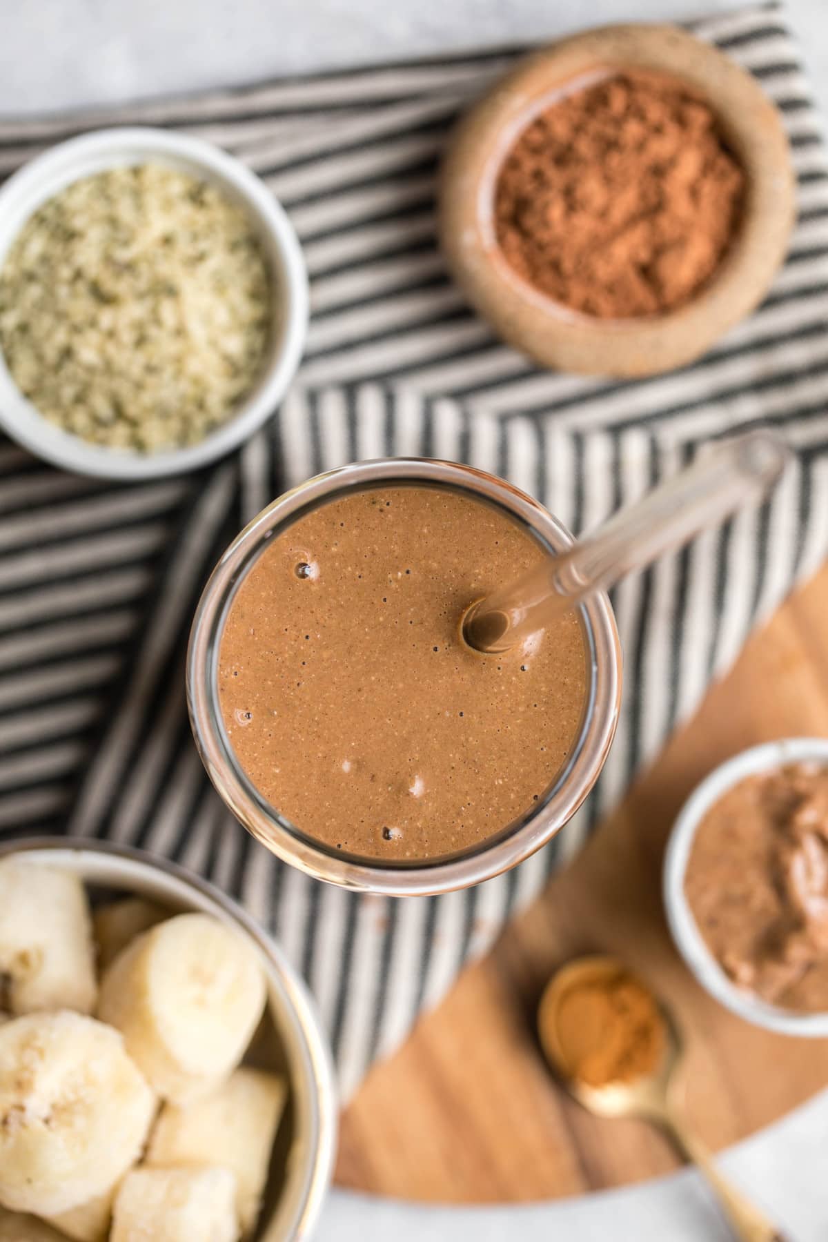 overhead shot of chocolate hemp smoothie in glass with straw on wood cutting board