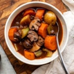 Bowl of vegan stew on wood cutting board with white linen on the side