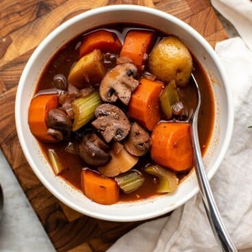 Bowl of vegan stew on wood cutting board with white linen on the side