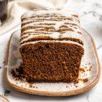gingerbread loaf topped with icing sugar slices on a white serving tray next to cups of coffee
