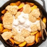 Grilled peach cobbler in cast iron pan with melted vanilla ice cream on top