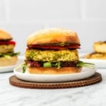 Grilled Pesto Tofu on a toasted roll with arugula, red peppers, and sundried tomatoes on white plate with marble background