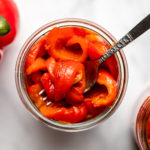 two glass jars of roasted red peppers with red pepper on marble background