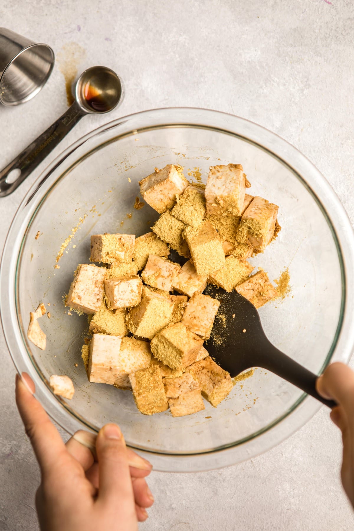 tossing tofu in nutritional yeast in large glass bowl