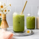 Two glasses of matcha latte with ice and gold straw