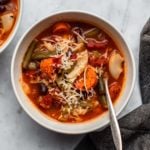 bowl of minestrone soup on marble background with grey napkin