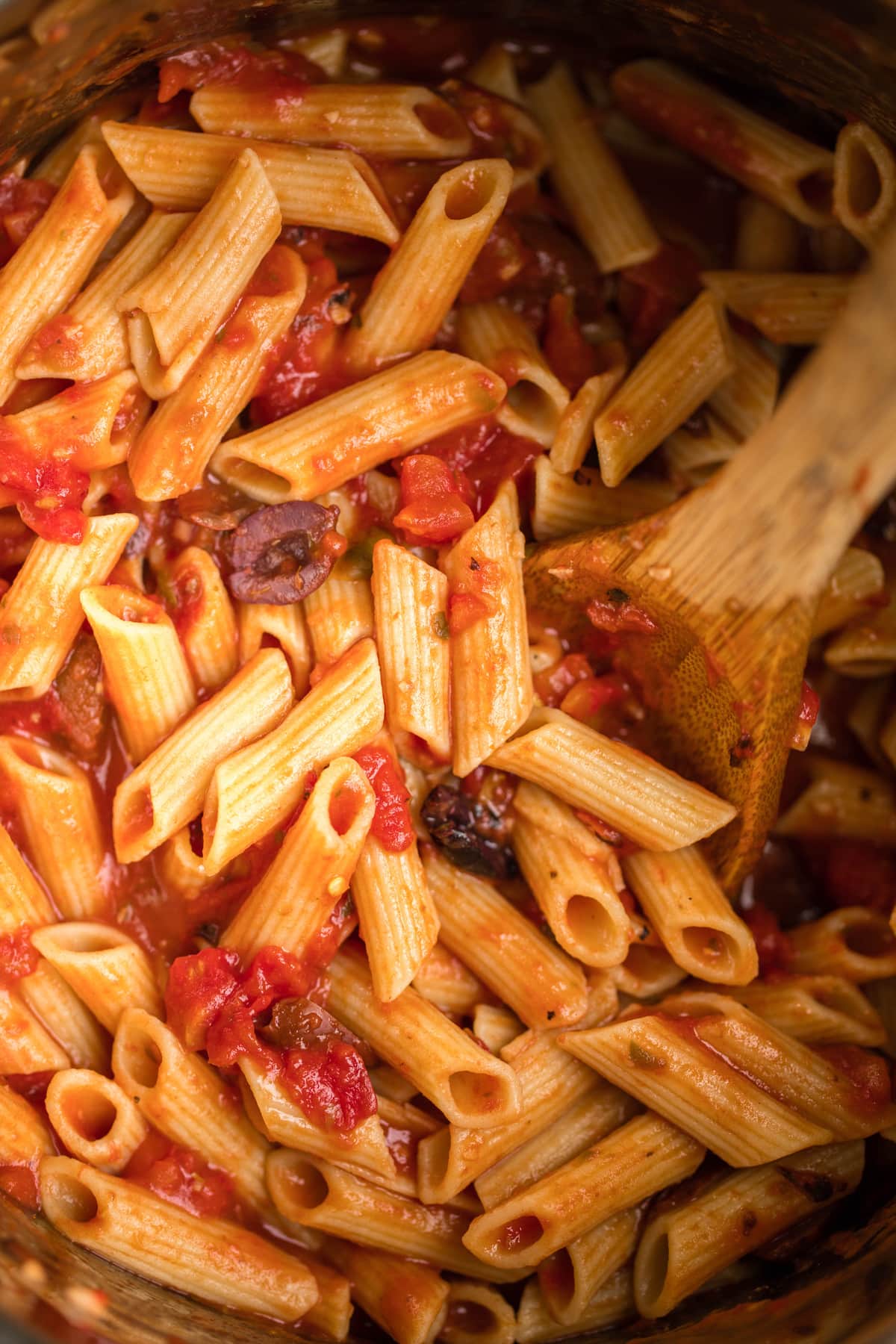 cooked penne puttanesca inside of instant pot with wooden spoon