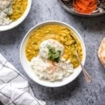 Two bowls of dal tadka with rice and raita on gray background