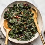 kale & cranberry salad tossed in tahini cider dressing in large white bowl topped with pecans and shallot