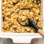 Lemon Dill Quinoa Casserole in white casserole dish with a wooden spoon scooping out the casserole. Small dished of fresh dill and green goddess dressing are off to the side.