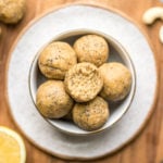 white bowl of lemon poppyseed energy bites on wood cutting board. bite is taken out of one ball