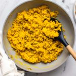 Cooked mung bean scramble in a medium-sized grey pan with a wooden spoon. A small bowl of mung beans sits off to one side, with a plate of toast on the other