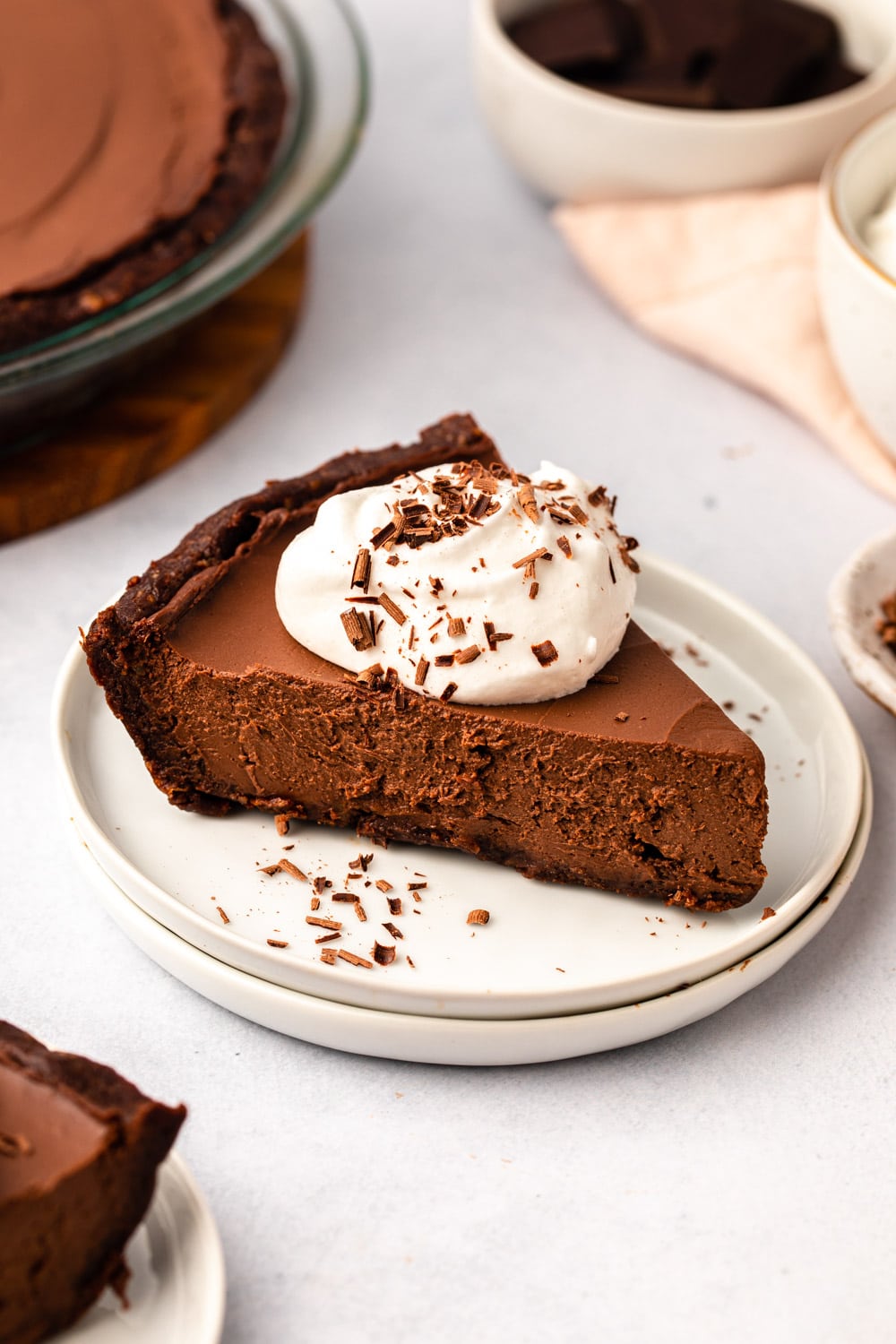 a slice of vegan chocolate pie served on a white plate and topped with coconut cream and chocolate flakes