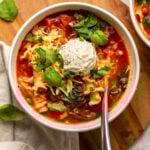 Two bowls of vegan lasagna soup topped with fresh herbs, vegan ricotta, and vegan mozzarella