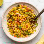 bowl of pan grilled corn salsa on tile background with limes on the side
