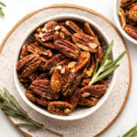 roasted rosemary pecans in small bowl with fresh rosemary
