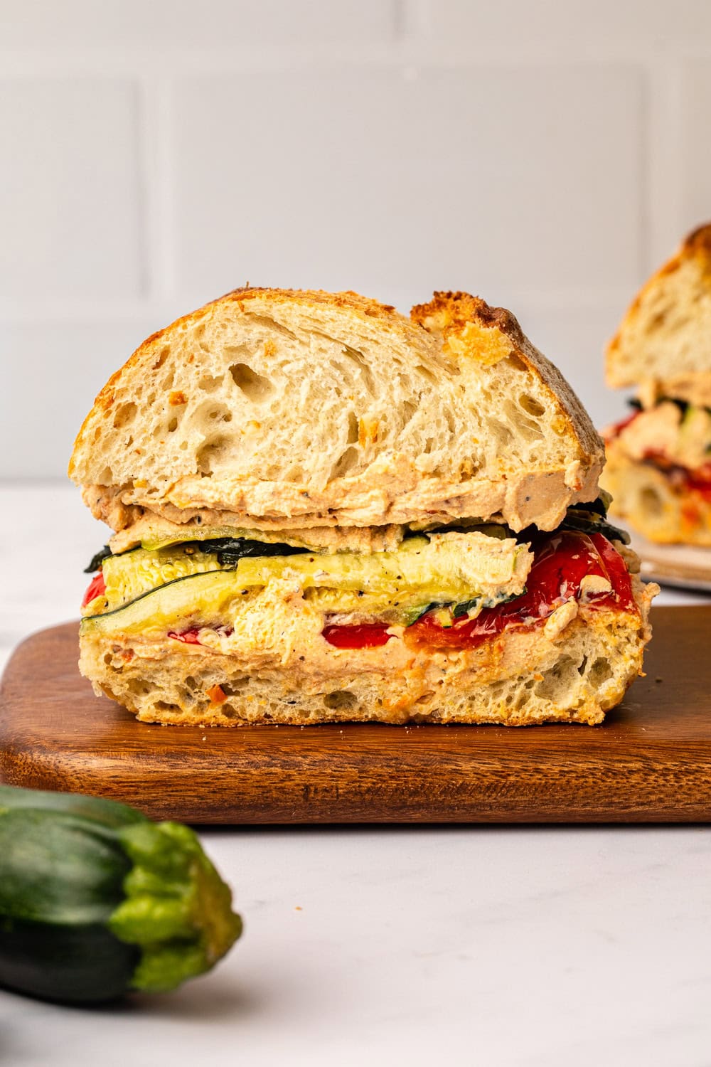 roasted zucchini sandwich cut in half placed on a cutting board with a zucchini placed aside on a marble kitchen countertop