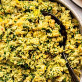 Spinach artichoke chickpea salad in white bowl with metal serving spoon
