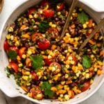 Overhead photo of Tex-Mex black bean salad in large bowl topped with fresh cilantro and gold serving spoons