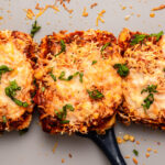 Baked tofu parmesan topped with vegan cheese and marinara sauce on baking sheet