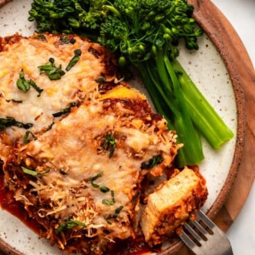 tofu parmesan on plate with steamed broccolini and bite taken out of it