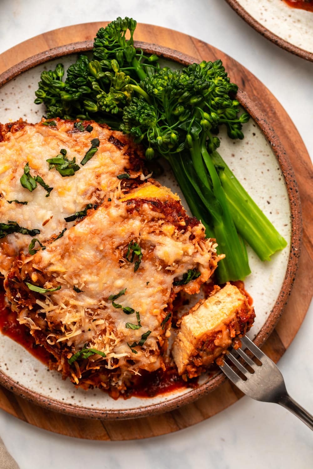 tofu parmesan on plate with steamed broccolini and bite taken out of it