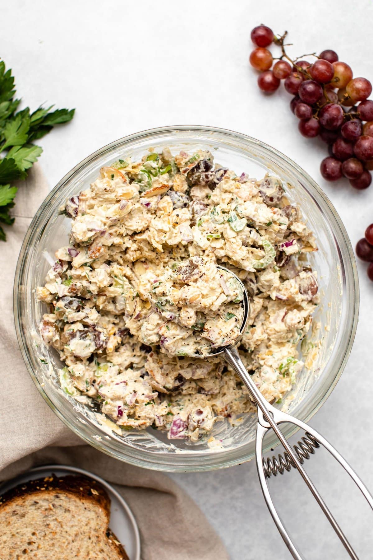 Chickpea salad in large glass bowl with metal scoop on marble background