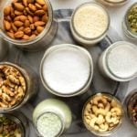 glass jars of nuts, seeds, and homemade nut milks on marble background
