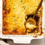 Vegan Shepherd's Pie with crispy golden potato crust in white casserole dish with gold serving spoon