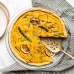 asparagus and mushroom quiche with slice taken out of it on marble background with striped napkin