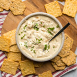 vegan french onion dip topped with parsley and black pepper on round wood serving tray