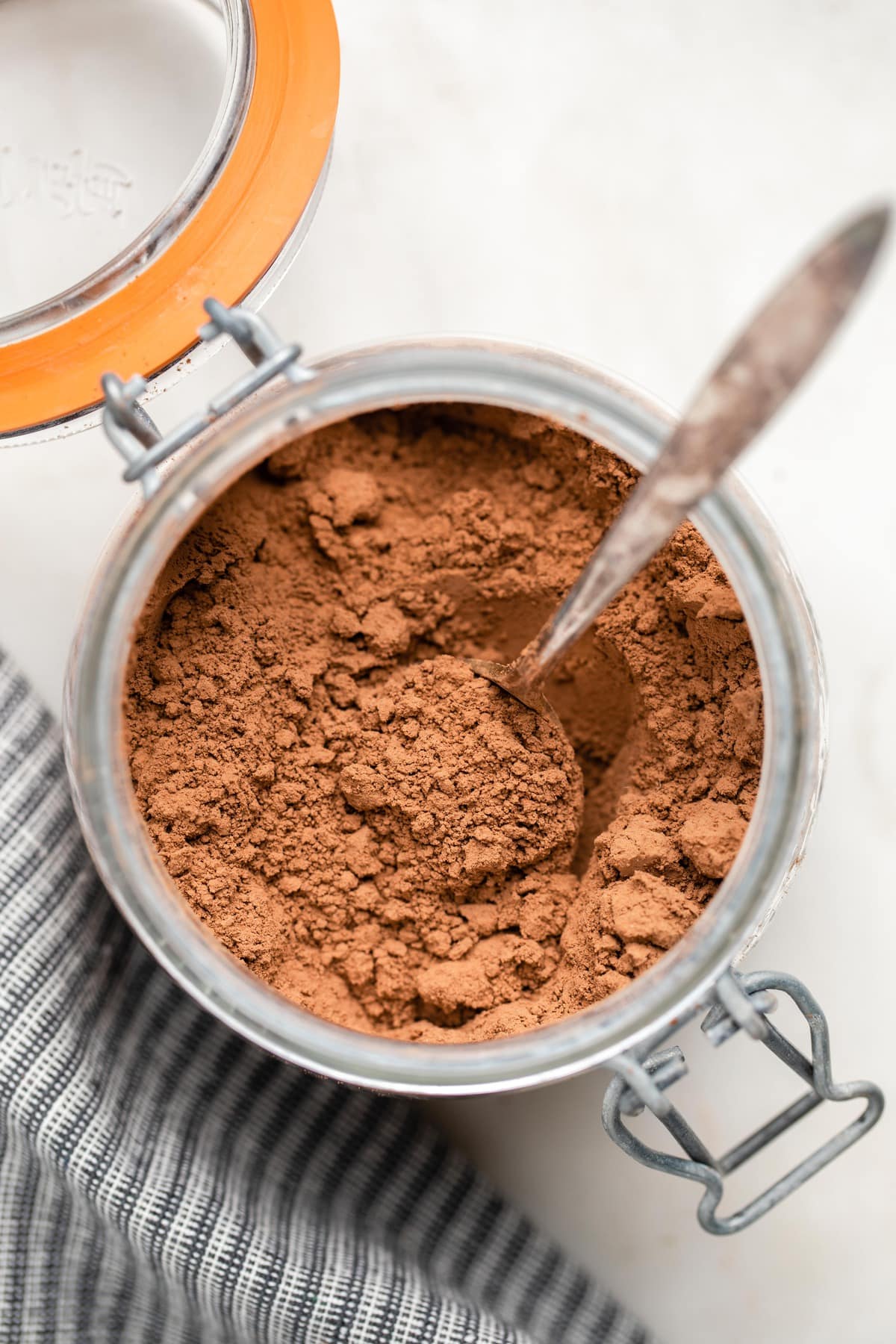 blended vegan hot cocoa mix in glass jar with metal spoon on white marble background