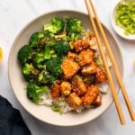 Orange tofu with broccoli and rice in bowl with chopsticks
