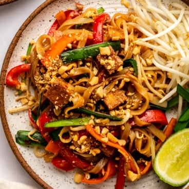 vegan pad thai on white plate topped with peanuts and with bean sprouts on the side
