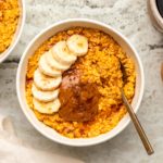 Bowl of pumpkin spice latte overnight oats in white bowl topped with banana, almond butter, and maple syrup