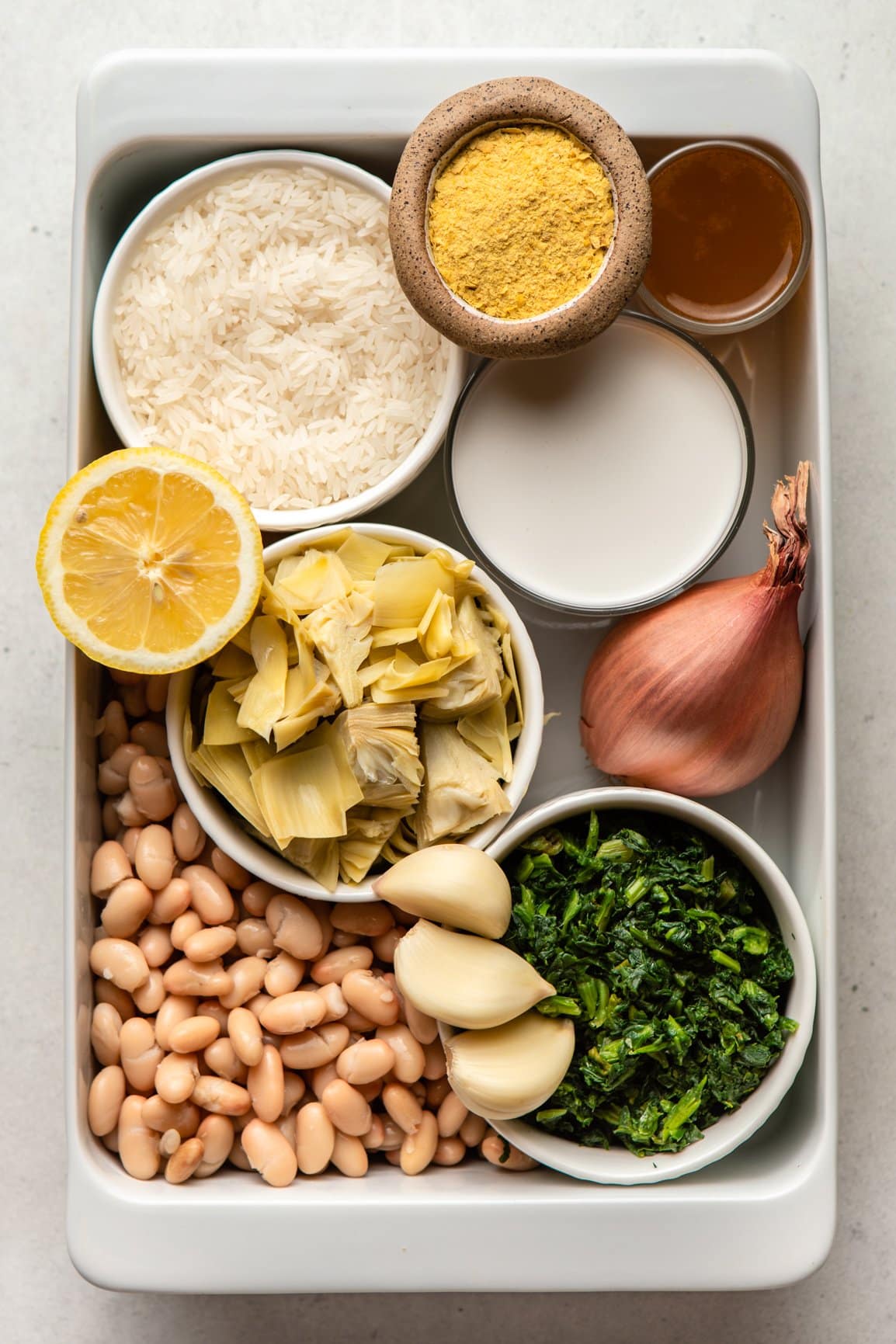 ingredients for vegan spinach and artichoke casserole in small white bowls arranged in casserole dish