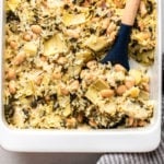 vegan spinach and artichoke casserole with wooden spoon in white casserole dish