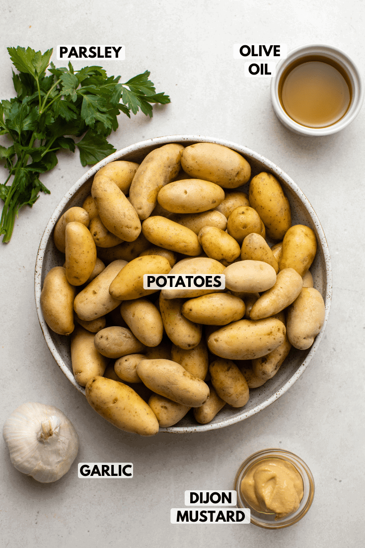 ingredients for potatoes on kitchen countertop. Clockwise text labels read olive oil, potatoes, dijon mustard, garlic, and parsley