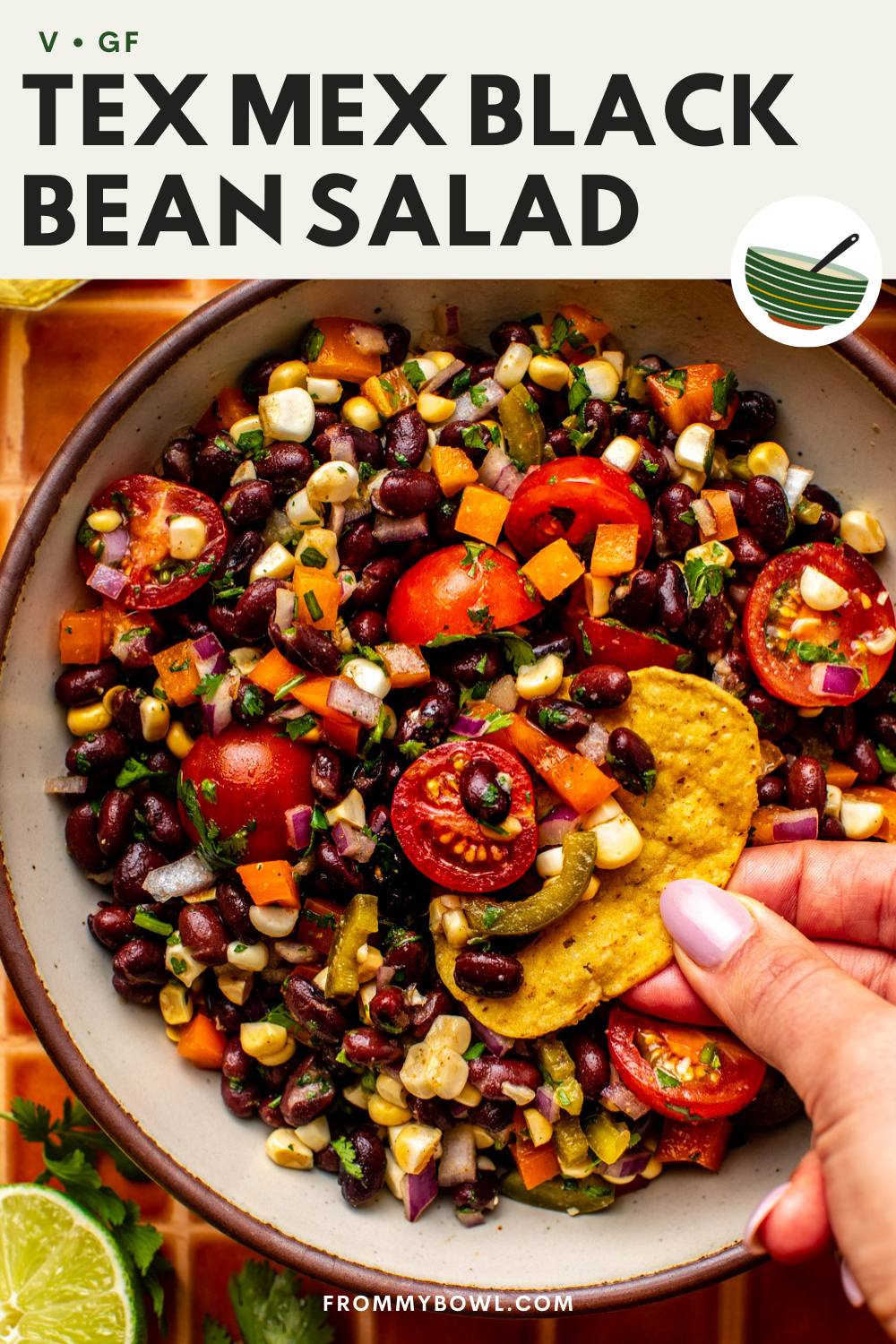 a tortilla chip scooping up a portion of the salad placed in an oval bowl on an orange checkered kitchen countertop